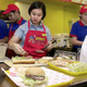 A waitress prepares a Spam hero, or submarine sandwich, in a bustling fast food restaurant.